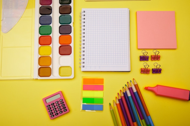 Cuaderno escolar y papelería sobre mesa amarilla. Fondo abstracto de regreso a la escuela