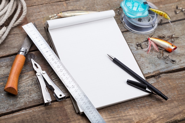 Cuaderno de escritura con aparejos de pesca y herramientas de diseño sobre tabla de madera.