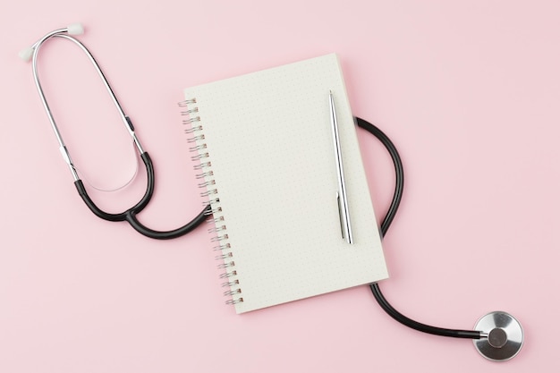 Cuaderno con estetoscopio sobre una mesa rosa