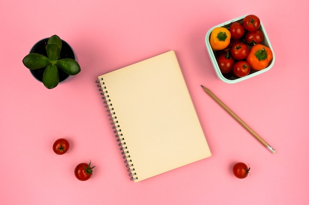 Cuaderno con flor de casa lápiz y contenedor con verduras sobre fondo rosa Top vie