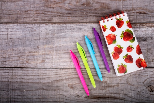 Cuaderno con fresas y set de lápices de colores sobre fondo de madera