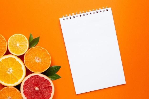 Cuaderno y frutas cítricas sobre fondo naranja