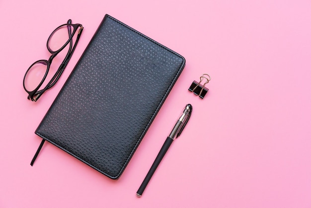 Cuaderno de gafas negras y temas de bolígrafo para capacitación y negocios sobre un fondo rosa regreso a la escuela