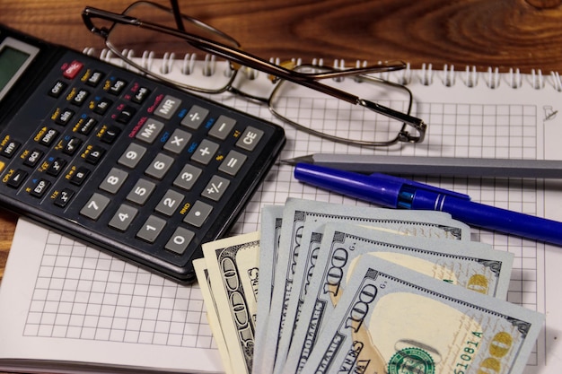 Cuaderno con gafas de pluma de dólares y calculadora en escritorio de madera Concepto financiero Contabilidad empresarial