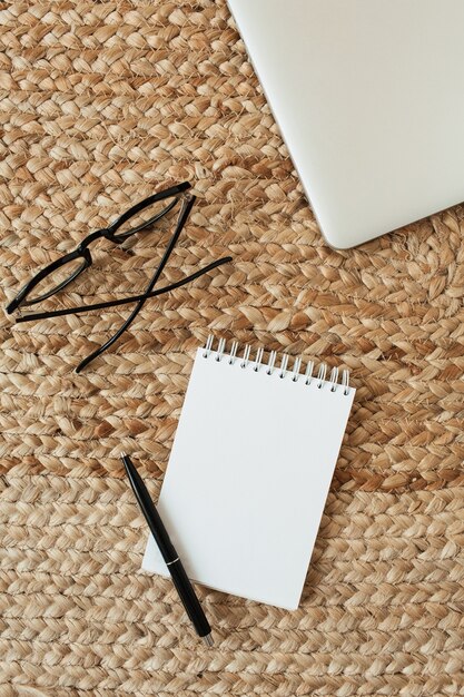 Cuaderno de hoja en blanco con espacio de copia, gafas, bolígrafo, portátil en paja de mimbre