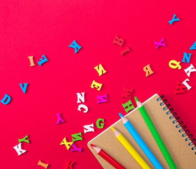 Cuaderno y lápices de madera multicolores sobre un fondo rojo