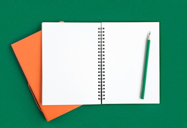 Cuaderno con lápiz. Cuaderno abierto sobre fondo de color verde oscuro, bloc de notas en espiral sobre la mesa. Vista superior del bloc de notas abierto con páginas en blanco, plano de oficina. Página blanca para su escritura. copia espacio