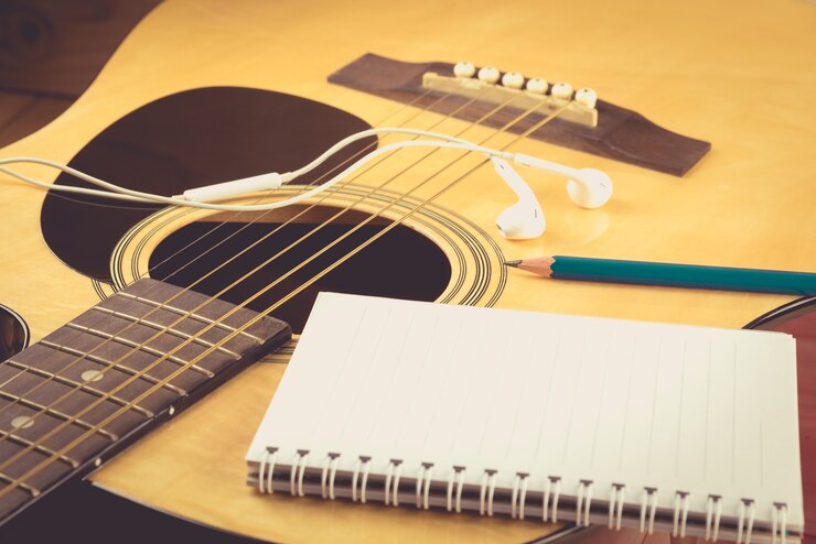 Foto cuaderno y lápiz en la guitarra, escribir música, vintage