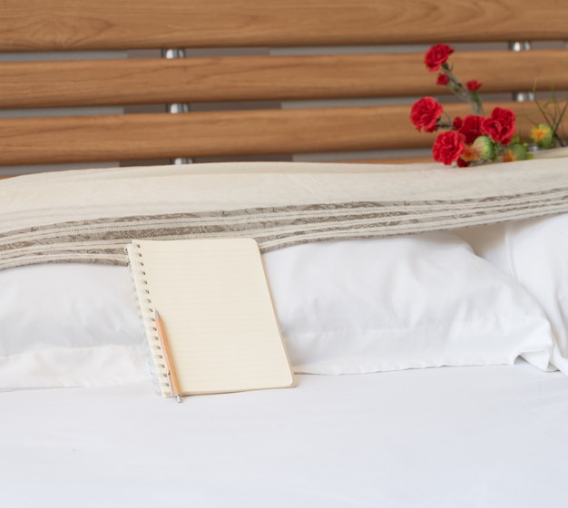 Foto cuaderno y lápiz de madera sobre cama blanca con ramo de flores