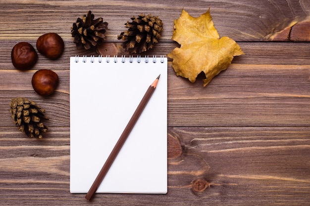 Cuaderno, lápiz y regalos de otoño sobre un fondo de madera.