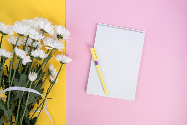 Un cuaderno limpio y un bolígrafo en una mesa rosa claro Mockup con un ramo de flores en una mesa amarilla