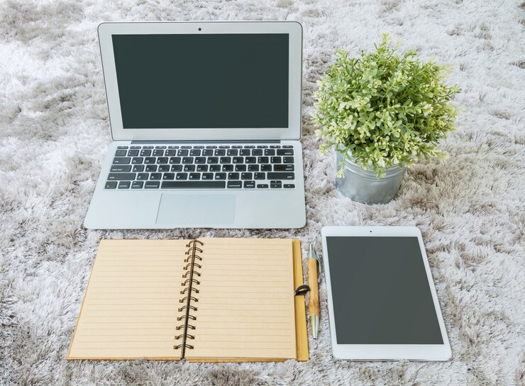 Foto el cuaderno marrón del primer, la pluma marrón, el cuaderno del ordenador, la tableta y la planta artificial en capet gris de la tela texturizaron el fondo