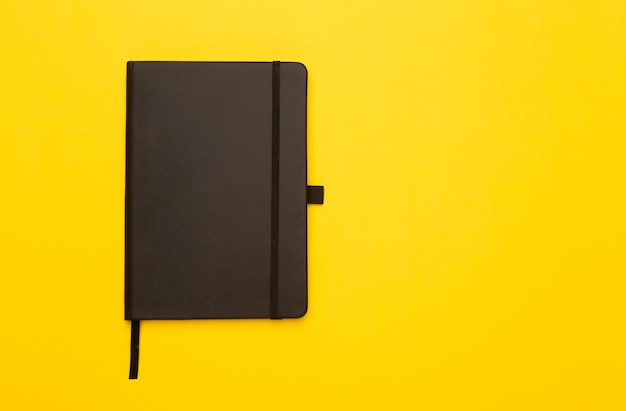 Cuaderno negro aislado en amarillo Flat lay o ángulo de visión superior.