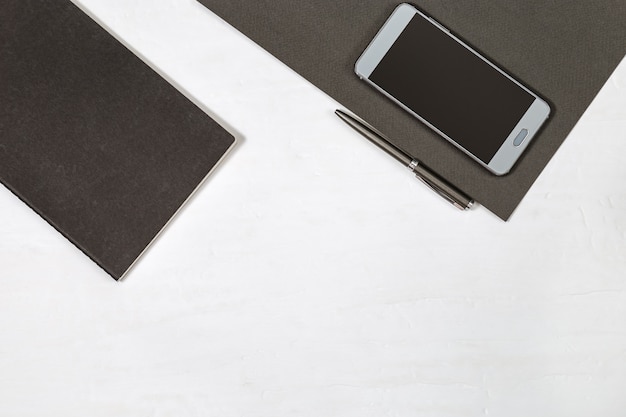 Cuaderno negro, pluma metálica gris, teléfono inteligente en la mesa. Concepto plano laico para la escuela o negocio. Vista superior con espacio de copia.