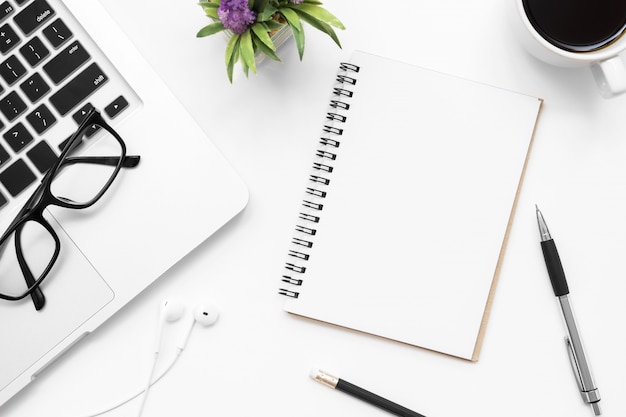 Foto cuaderno con la página en blanco está en la mesa de escritorio de oficina blanca con suministros. vista superior, aplanada.