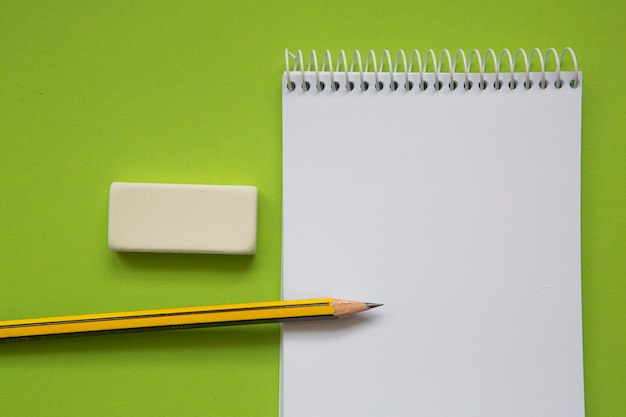 Cuaderno con una página en blanco sobre un fondo verde pistacho y junto con un lápiz y varios st