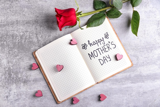 Cuaderno con palabras Feliz día de la madre y rosa roja sobre fondo gris