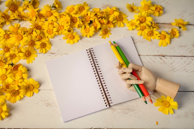 Foto cuaderno de papel blanco entre flores, lápices y bloc de notas con cierre elástico