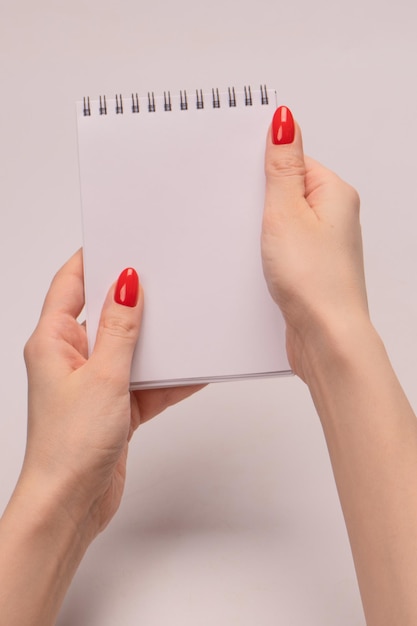 Un cuaderno con papel blanco vacío en manos de mujer con uñas rojas