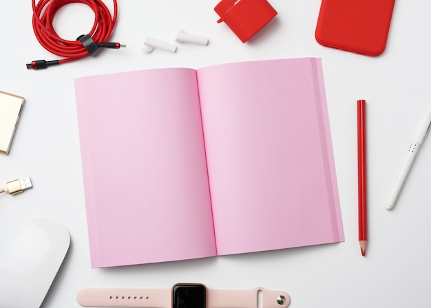 Cuaderno de papel rosa, banco de energía con cable, teléfono inteligente rojo, auriculares, mouse inalámbrico y reloj inteligente