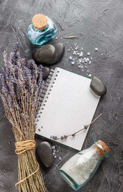 Cuaderno pequeño, lavanda, sal marina mineral y piedras zen sobre un fondo de piedra gris.