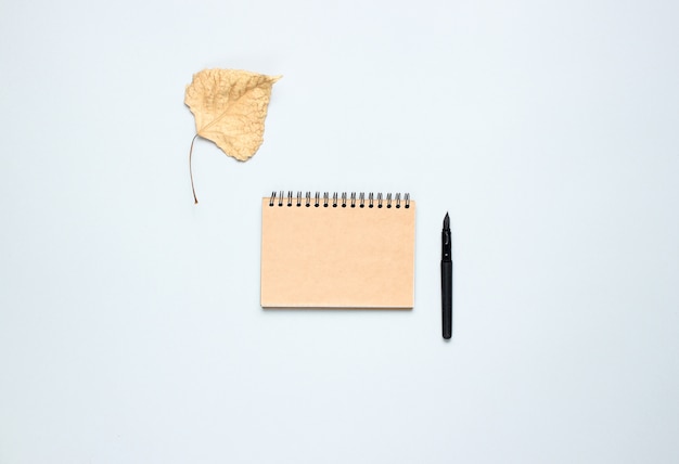 Cuaderno con pluma, hojas de otoño caídas sobre una mesa gris. Otoño de inspiración, escritura. Vista superior, minimalismo. Lay Flat