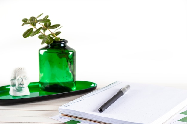 Cuaderno, pluma y planta en maceta sobre fondo de madera.