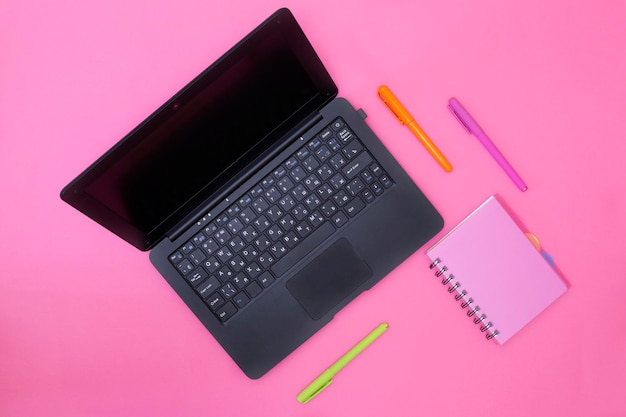 Cuaderno portátil y bolígrafos sobre un fondo rosa.
