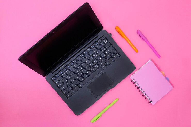 Foto cuaderno portátil y bolígrafos sobre un fondo rosa.