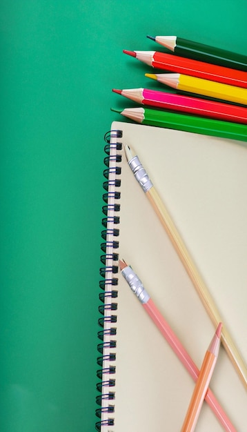 Cuaderno de primer plano y lápices de colores sobre un fondo de tablero verde