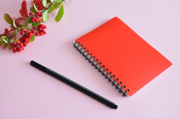 cuaderno rojo con bolígrafo negro y rama de agracejo con bayas rojas y hojas de otoño