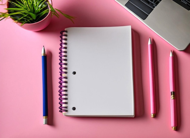 Un cuaderno rosa con un bolígrafo azul junto a un portátil.