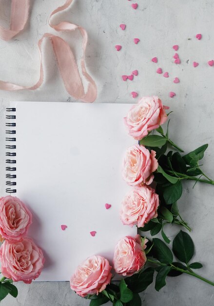 Cuaderno rosas cinta rosa y caramelos dulces en forma de corazón sobre fondo blanco Decoración para San Valentín o tarjeta del día de la boda vista superior plana enfoque selectivo