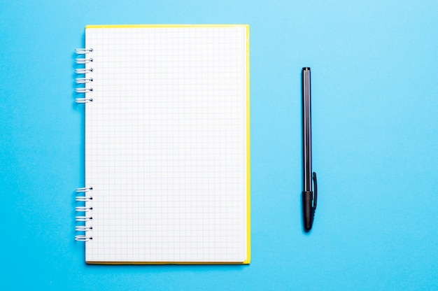 Cuaderno sobre un fondo azul con bolígrafos.