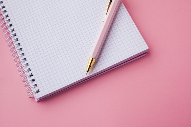 Cuaderno con tapa de plástico color rosa, bolígrafo y clips. fondo rosa enfoque selectivo