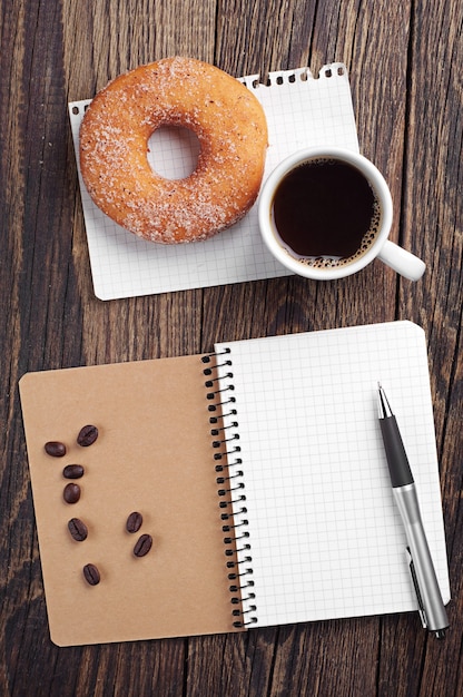 Cuaderno y taza de café con donut en mesa de madera antigua