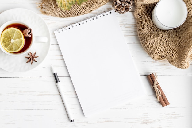 Cuaderno, té caliente, pluma, vela en una mesa de madera blanca. Bosquejo