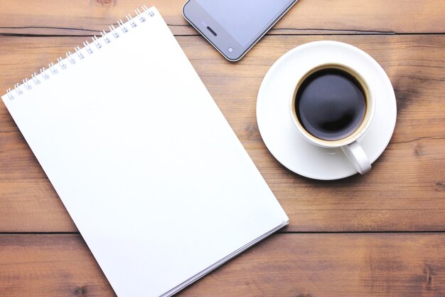 cuaderno, teléfono y café en la mesa de madera