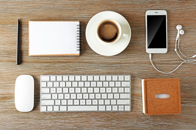 Cuaderno de teléfono con teclado y taza de café en una vista superior de fondo de escritorio de madera