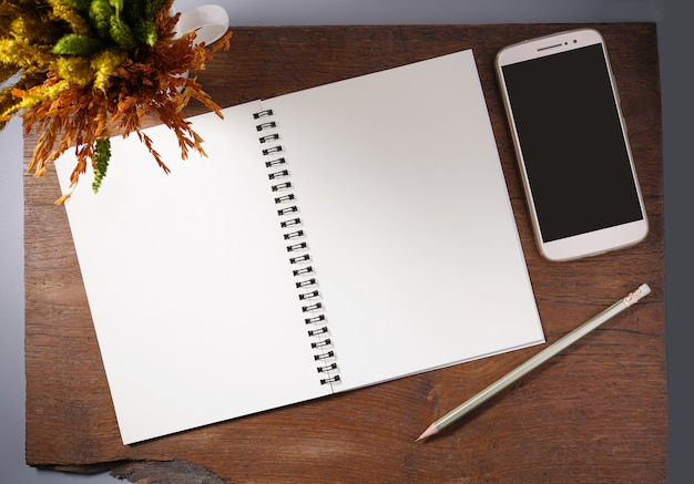 Cuaderno vacío con el lápiz, el smartphone y la flor seca en la tabla de madera.