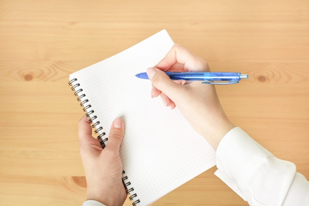 Cuaderno vacío y mano femenina con lápiz sobre escritorio de madera.