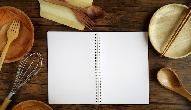 Cuaderno de la vista superior para escribir la receta del menú y los  utensilios de cocina de madera que cocinan las herramientas en el fondo de  madera de la tabla.