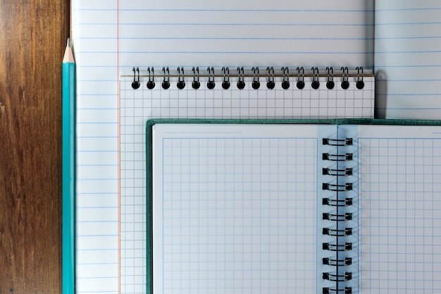 Cuadernos en blanco abiertos con hojas blancas en una regla y una caja en un primer plano de fondo de madera marrón