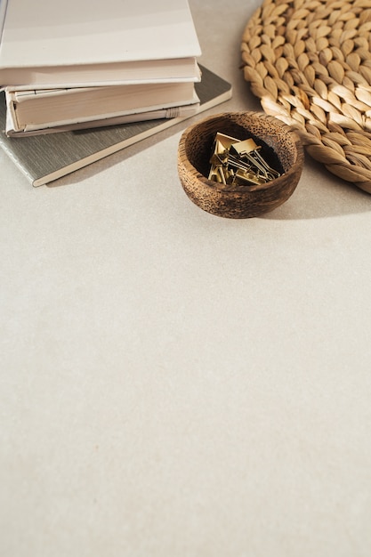 Cuadernos, clips en cuenco de madera, soporte de paja sobre hormigón beige