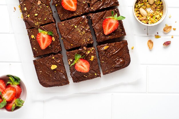 Cuadrados de chocolate con pistachos y fresas sobre papel blanco