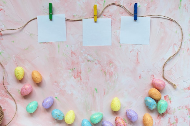 Cuadrados de papel en blanco clavados en una cuerda y decoración de huevos de color pastel y dorado sobre un fondo rosa Celebración de Pascua y concepto de lista de tareas Vista superior espacio de copia plana