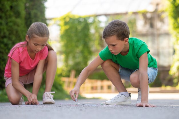 Cuadro. Niño y niña en edad escolar primaria enfocados en serio dibujo con lápices de colores en el parque en un día caluroso