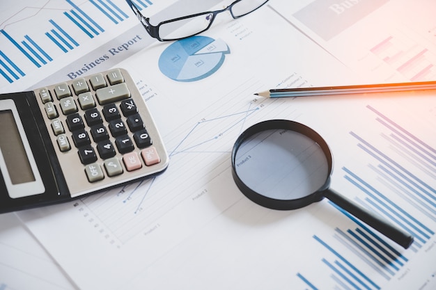 cuadros y gráficos con lupa y lápiz, calculadora, reloj. Luz de reflejo y destello. Imagen de concepto de recopilación de datos y trabajo estadístico.