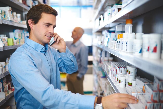 ¿Cuál es el nombre otra vez? Captura recortada de un apuesto joven que hace una llamada telefónica mientras busca medicamentos en una farmacia.