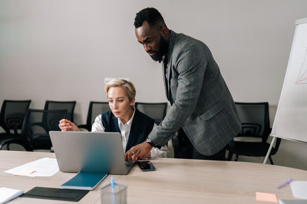 Cualificada de mediana edad mujer caucásica CEO gerente ejecutivo con traje mentoring joven africano